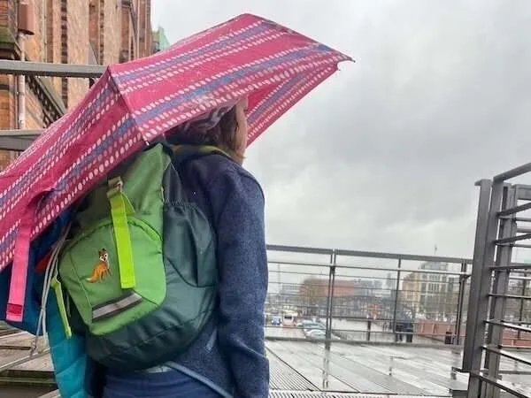 Kind Regenschirm und Rucksack bei Regenwetter in Stadt.