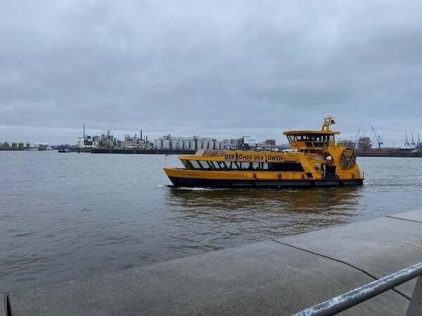Ein gelbes Passagierschiff fährt auf der Elbe in Hamburg, bei bewölktem Himmel, mit industriellen Gebäuden im Hintergrund, ideal für kreative Familienfotos oder Hafenbesichtigungen.