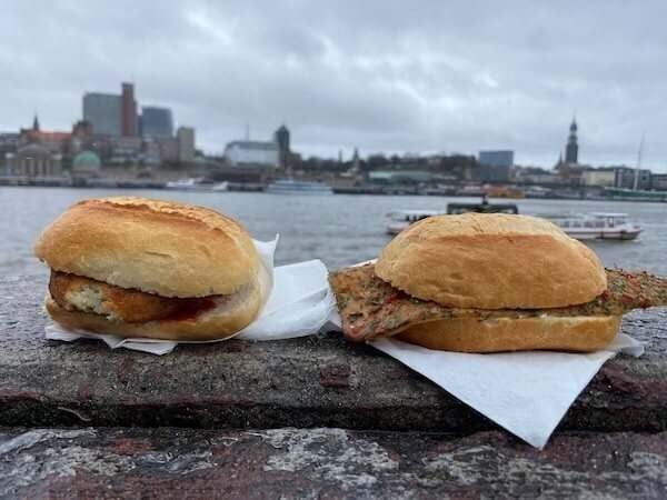 Zwei belegte Brötchen vor einer Stadt- und Flusskulisse, perfekte Genussmomente in der Stadt.