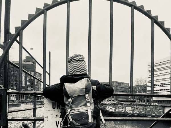Kind steht vor einem großen eisernen runden Tor mit Schiffen im Hintergrund