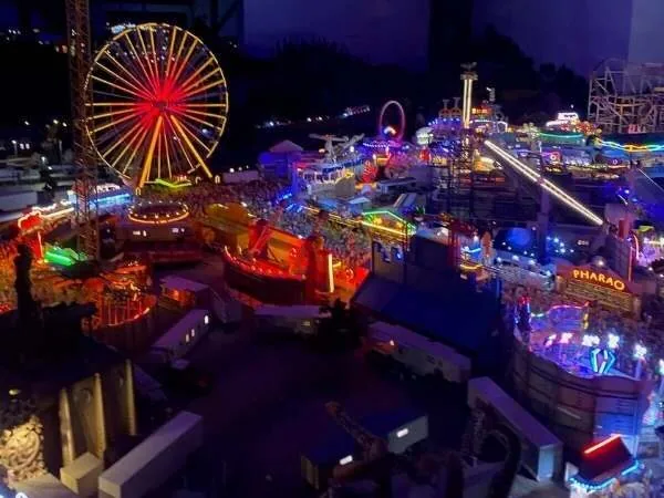 Bunte, leuchtende Kirmes bei Nacht mit Achterbahnen, Riesenrad und Fahrgeschäften, ideal für Familien und Freizeitpark-Enthusiasten.