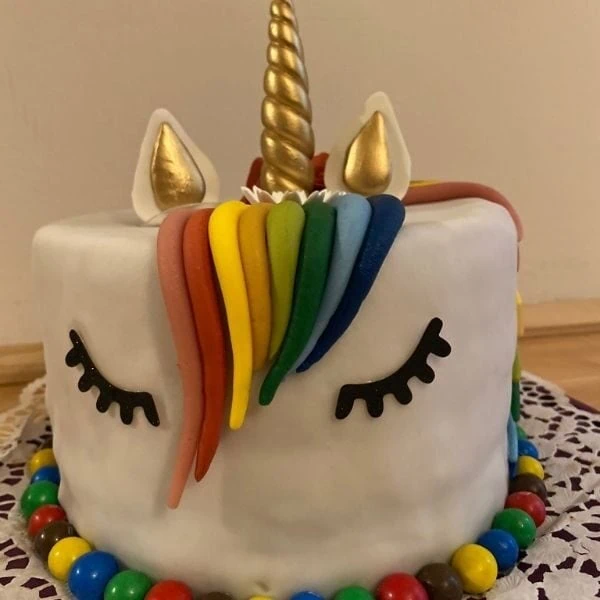 Torte in Form von einem Einhorn mit Fondant Mähne und hörn und Smarties am Boden um die Torte