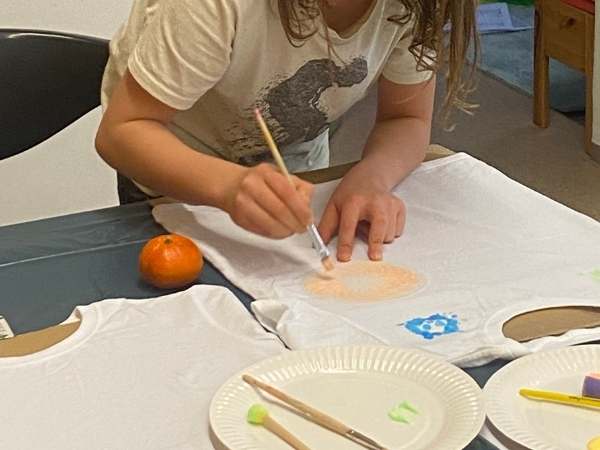 Junge Bastlerin gestaltet eine T-Shirt-Applikation mit Farbe, umweltfreundlich und spa&szlig;ig f&uuml;r Kinder, kreative Besch&auml;ftigung, DIY Modeprojekt, MamaBlog Ideen, nachhaltiges Basteln.