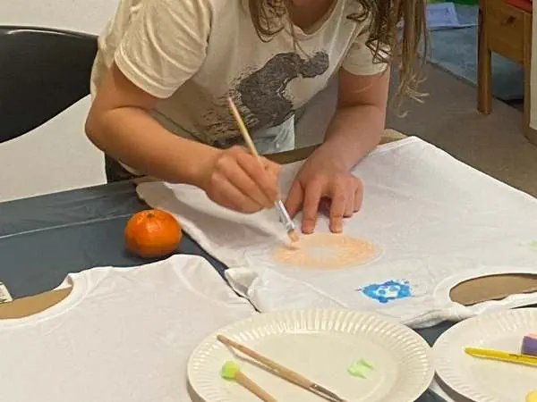 Junge Bastlerin gestaltet eine T-Shirt-Applikation mit Farbe, umweltfreundlich und spaßig für Kinder, kreative Beschäftigung, DIY Modeprojekt, MamaBlog Ideen, nachhaltiges Basteln.