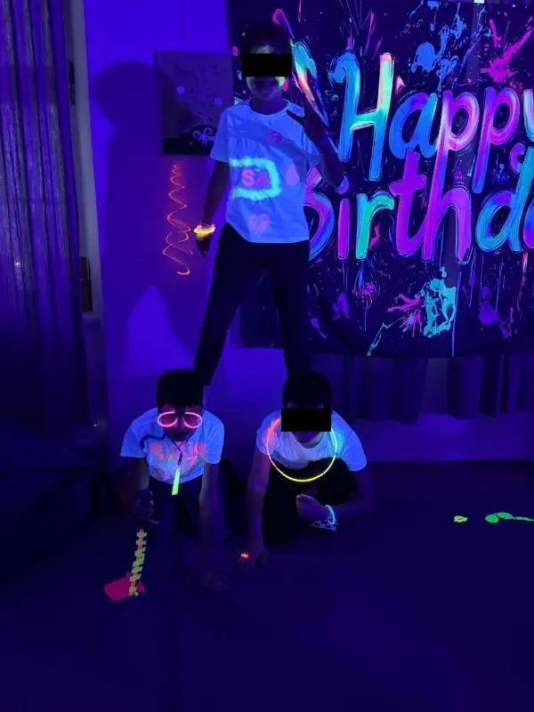 Kinder mit leuchtenden Accessoires bei Kindergeburtstag in dunklem Raum.