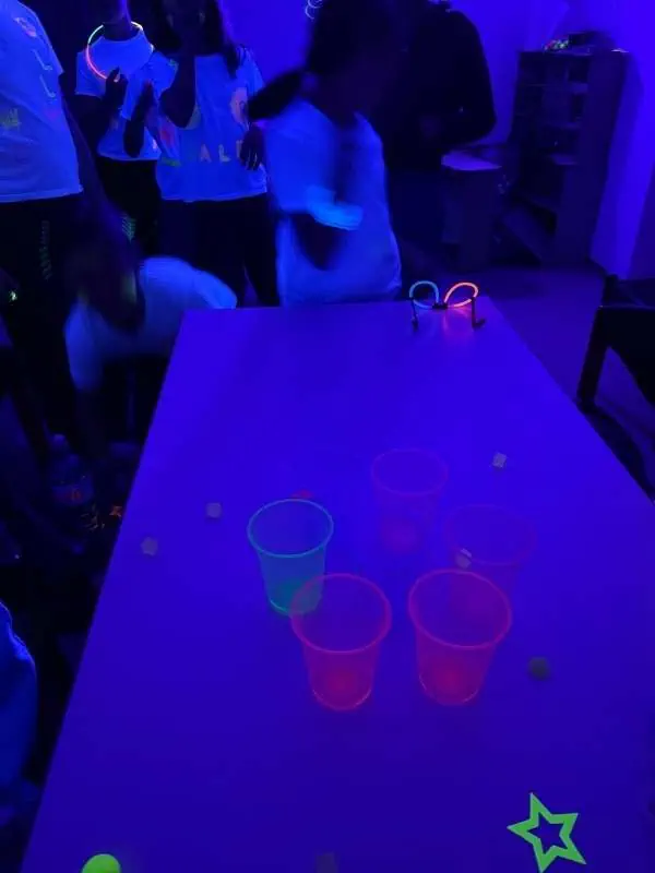 Bunte fluoreszierende Getränke und Lichter im dunklen Raum, Kinder spielen und lassen sich von UV-Licht faszinieren, perfekte Atmosphäre für Partys und Kindergeburtstage.