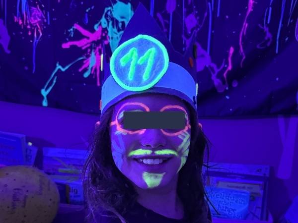 Kind mit fluoreszierender Schminke im UV-Licht mit einer Krone mit einer leuchtenden 11