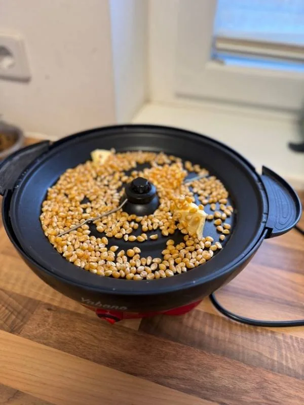 Alte Popcornmaschine mit Maiskörnern zum Selbermachen, ideal für gemütliche Fernsehabende oder Partys, einfache Handhabung, schnelle Zubereitung.