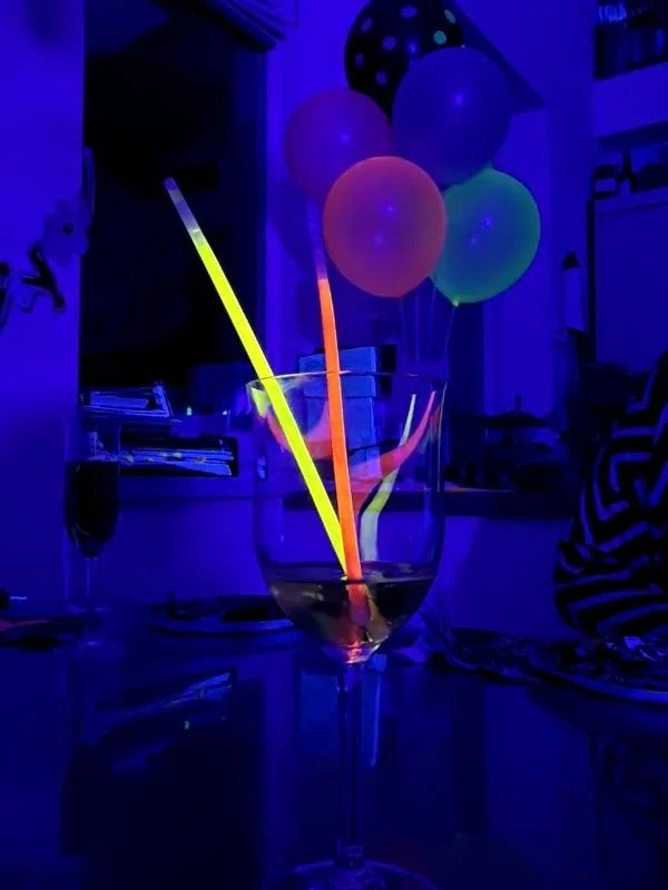 Leuchtende Ballons und Trinkhalme in einem Glas, ideal für Party und Feierlichkeiten, auch bei Dunkelheit, mit einem neonartigen Glühen und festlicher Atmosphäre.