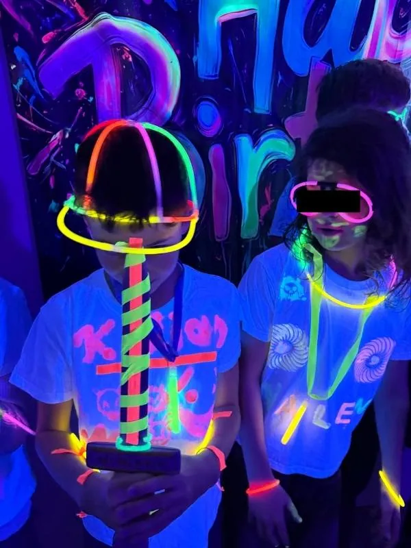 Kinder tragen fluoreszierende Brillen und Leuchtarmbänder auf Neon-Party, leuchtende Farben und Spaß bei Nachtveranstaltung entdecken.