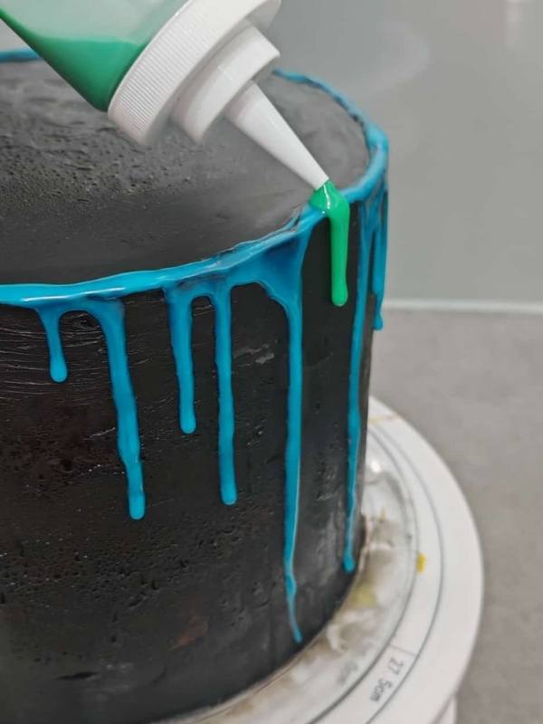 Ein schwarzer Kuchen mit blauer Glasur, die dekorativ herunterl&auml;uft, und gr&uuml;ner Zuckerschrift, perfekt f&uuml;r Kindergeburtstag oder Feierlichkeiten.