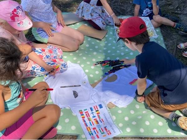 Kinder sitzen auf dem Boden und malen ihre Fußballshirts an