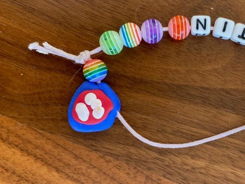 Bunte Perlen und ein Schnulleranhänger auf Holzoberfläche, Babyzubehör, kindgerechtes Accessoire, ideal für Babys und Kleinkinder, handgemacht, farbenfrohes Design, Babygeschenk, MamaBlog.