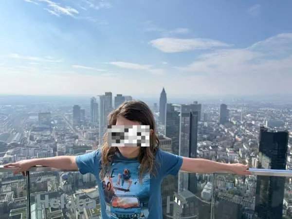 Hoch oben auf einem Wolkenkratzer in New York City mit Blick auf die Skyline, eine junge Frau mit offenen Armen, die Stadt im Hintergrund, sonniger Tag, urbane Aussicht, Lifestyle, Reisen, Freiheit.