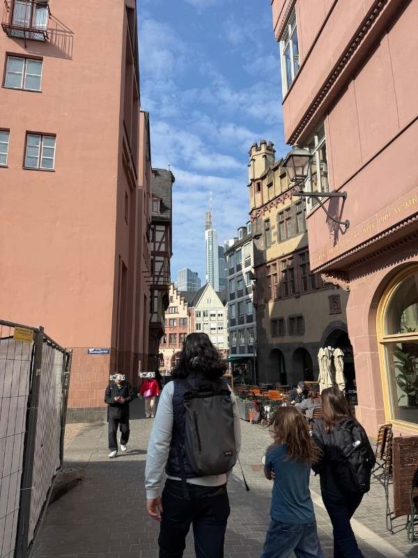 Einkaufsstra&szlig;e in einer historischen Stadt mit modernen Hochh&auml;usern im Hintergrund, Menschen beim Spaziergang, sonniger Tag, lebendige Atmosph&auml;re, Stadtleben, urbane Umgebung.