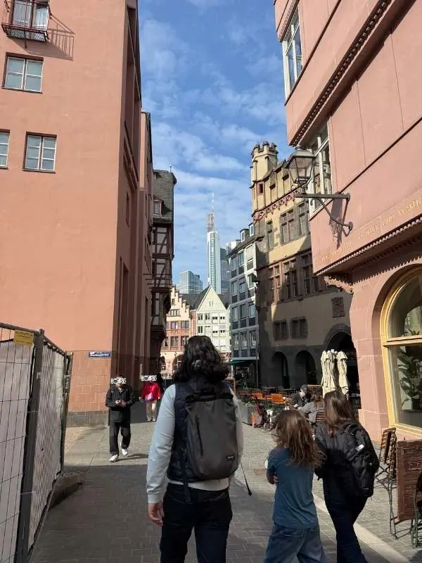 Einkaufsstraße in einer historischen Stadt mit modernen Hochhäusern im Hintergrund, Menschen beim Spaziergang, sonniger Tag, lebendige Atmosphäre, Stadtleben, urbane Umgebung.
