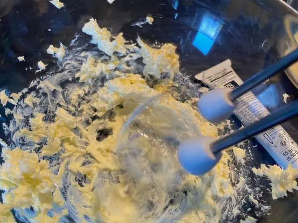 Buttercreme-Frosting wird mit einem Handmixer in einer Schüssel geschlagen, um eine cremige Konsistenz für Kuchen und Desserts zu erzielen.