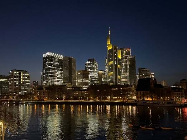Der Nachthimmel &uuml;ber der Skyline von Frankfurt am Main mit beleuchteten Wolkenkratzern und reflektierenden Lichtern im Fluss, Stadtbild bei Nacht, moderne Architektur, urbanes Leben.