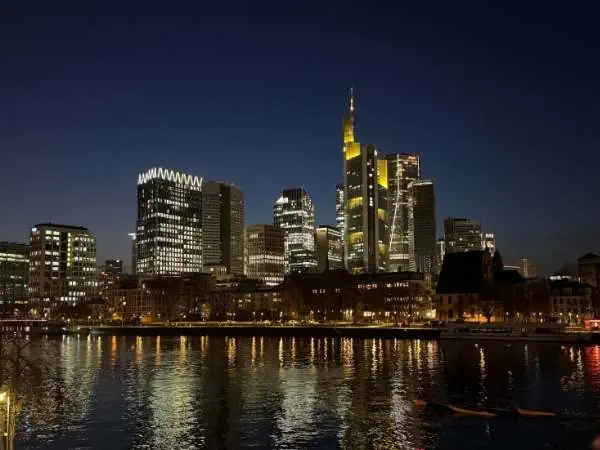 Der Nachthimmel über der Skyline von Frankfurt am Main mit beleuchteten Wolkenkratzern und reflektierenden Lichtern im Fluss, Stadtbild bei Nacht, moderne Architektur, urbanes Leben.