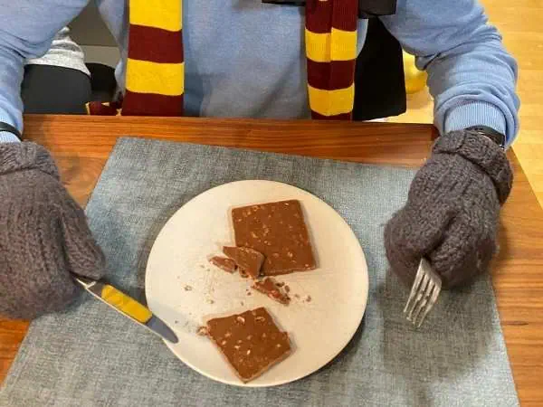 Ein Kind mit grauen Handschuhen isst Schokolade auf einem weißen Teller, passend zum Thema kooperative Spiele für Kindergeburtstage, ohne Wettkampf.