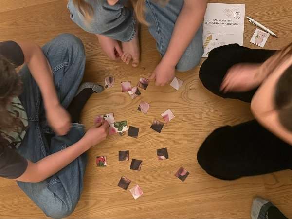 Ein Kind spielt mit Puzzleteilen auf einem Holzboden, w&auml;hrend andere Kinder zuschauen, im Rahmen einer Schatzsuche f&uuml;r Kinder, drinnen oder drau&szlig;en, bei einer Schnitzeljagd.sie ein Puzzle Puzzle