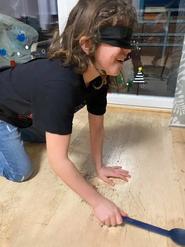 Kind auf dem Boden mit einer Augenbinde und einem Kochlöffel in der Hand