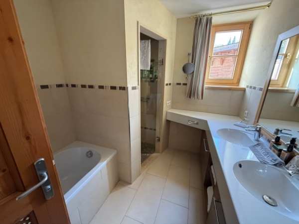 Ein modernes Badezimmer mit Badewanne, Doppelwaschbecken, großem Spiegel, natürlichem Licht durch Fenster, ideal für Familien und Komfort.