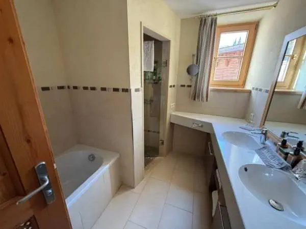 Ein modernes Badezimmer mit Badewanne, Doppelwaschbecken, großem Spiegel, natürlichem Licht durch Fenster, ideal für Familien und Komfort.