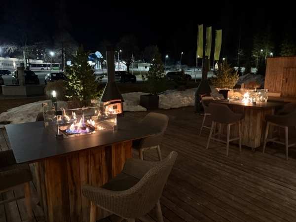 Gemütliche Outdoor-Terrasse bei Nacht mit Feuerstellen, Sitzgelegenheiten und winterlicher Dekoration, ideal für entspannte Abende im Freien.