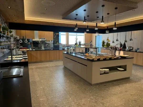Frühstücksbuffet in einem modernen Hotelrestaurant mit Holzdekoration, großen Fenstern und vielfältigen Speisen auf einem zentralen Tisch, ideal für Familien und Geschäftsreisende.