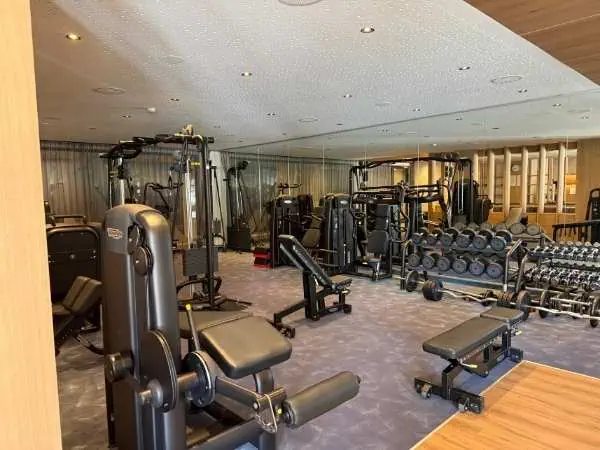 Ein modernes Fitnessstudio mit verschiedenen Kraft- und Ausdauergeräten, Hanteln und Trainingsbänken in einer hellen, gut ausgestatteten Umgebung.