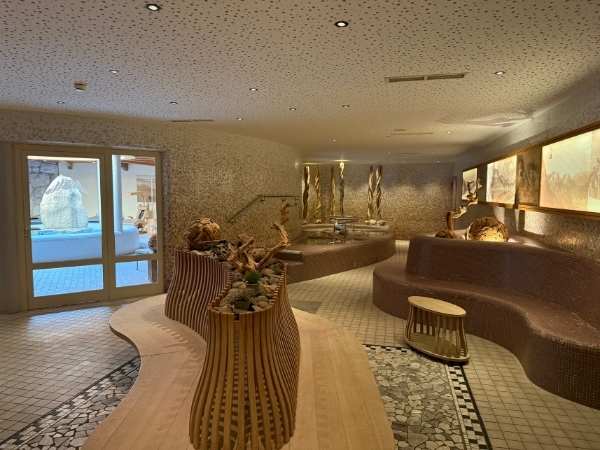 Entspannter Wellnessbereich mit Sitzgelegenheiten, Wasserbrunnen und warmem Licht in einem modernen Spa- oder Hotelraum, ideal für Erholung und Entspannung.