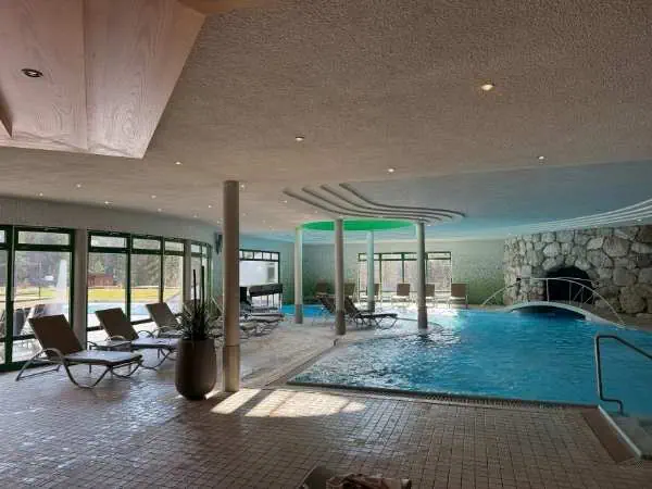 Entspannter Innenpoolbereich in einem modernen Spa mit Liegestühlen, großen Fenstern und natürlichem Licht, ideal für Erholung und Wellness.