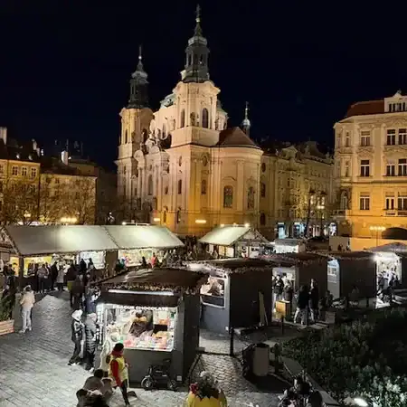 Bunte Marktstände auf einem nächtlichen Stadtplatz vor einer historischen Kirche mit beleuchteten Türmen, lebendige Atmosphäre, Menschen beim Einkaufen und Flanieren, urbanes Stadtbild, festliche Stim.