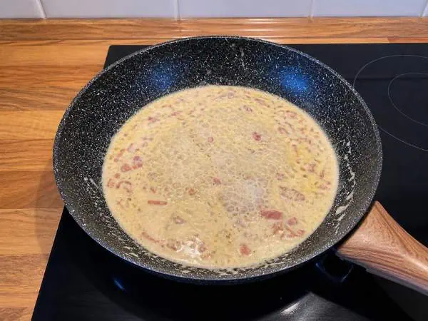 Brennendes Ei in einer schwarzen Pfanne auf einem Herd, ideal für Kochrezepte und Familienküche, Fokus auf Zubereitung von Eierspeisen, Küchenutensilien, gesunde Ernährung.