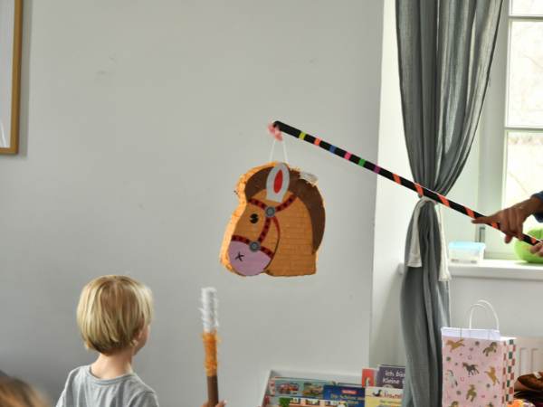 Ein Kind spielt mit einer selbstgemachten Angel aus Papier und Strohhalm, um ein buntes, handgefertigtes Fischtier in einem Wohnzimmer zu fangen, f&ouml;rdert Kreativit&auml;t und Feinmotorik bei Kindern.