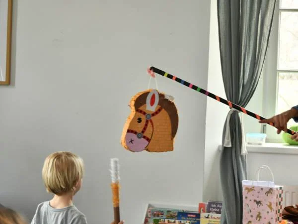Ein Kind spielt mit einer selbstgemachten Angel aus Papier und Strohhalm, um ein buntes, handgefertigtes Fischtier in einem Wohnzimmer zu fangen, fördert Kreativität und Feinmotorik bei Kindern.