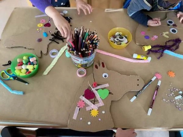 Buntes Bastelbild eines Kindergeburtstags mit Kindern, die ein Steckenpferd aus Papier, Filz und Dekorationen für eine kreative Bastelaktivität herstellen.