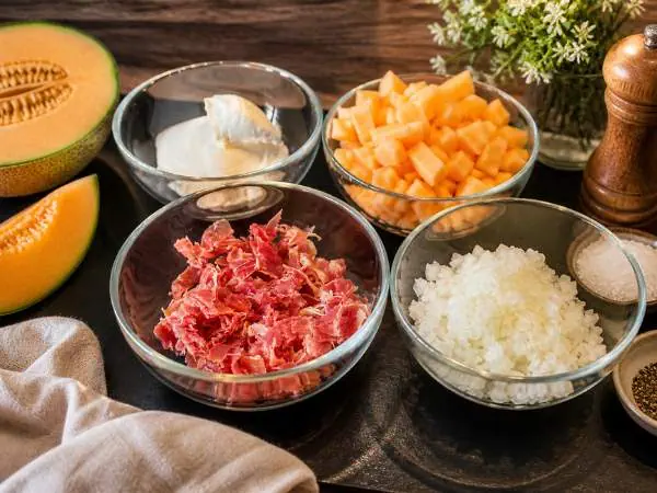 Frisches Hackfleisch, gewürfelter Kürbis, Quark, geriebener Käse und weitere Zutaten in Schüsseln für ein gesundes Familienessen, auf dunklem Holzbrett, natürliche Beleuchtung, Mama-Blog-Inspiration.