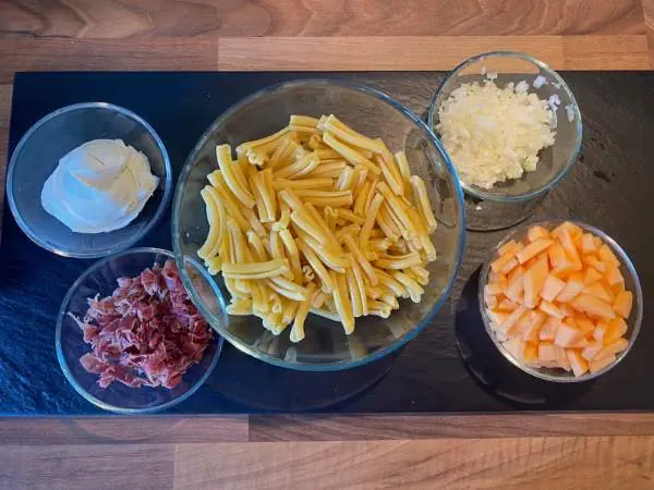 zutaten für das außergewöhnliche Licht Nudelgericht in Schalen auf einem Tisch: Nudeln, Zwiebel, Schinken, Melonen, Mascarpone