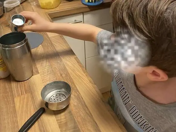 Kind dosiert Zutaten für einen Kindercocktail am Tisch