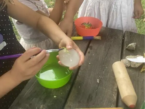 Kind befreit einen kleinen Dinosaurier mit Pinsel und Wasser aus einem Eisball