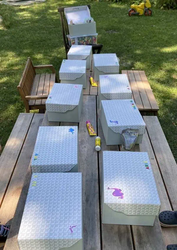 Vorbereitete Bastelboxen mit Namen auf dem Tisch für die Dino-Landschaft am Kindergeburtstag