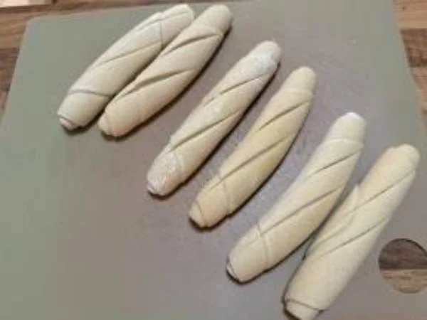 Frischer, roher Teig in Strängen, bereit zum Formen für Gebäck oder Brot, auf einer Küchenarbeitsfläche.