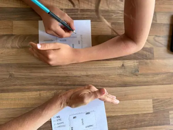Kind und Erwachsener spielen mit Stift auf kariertem Papier