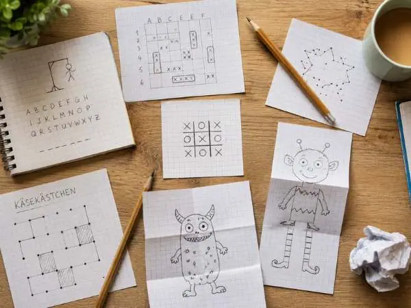 Verschiedene Spiele mit Stift und Papier auf einem Tisch, darunter Galgenmännchen, Käsekästchen und Tic Tac Toe