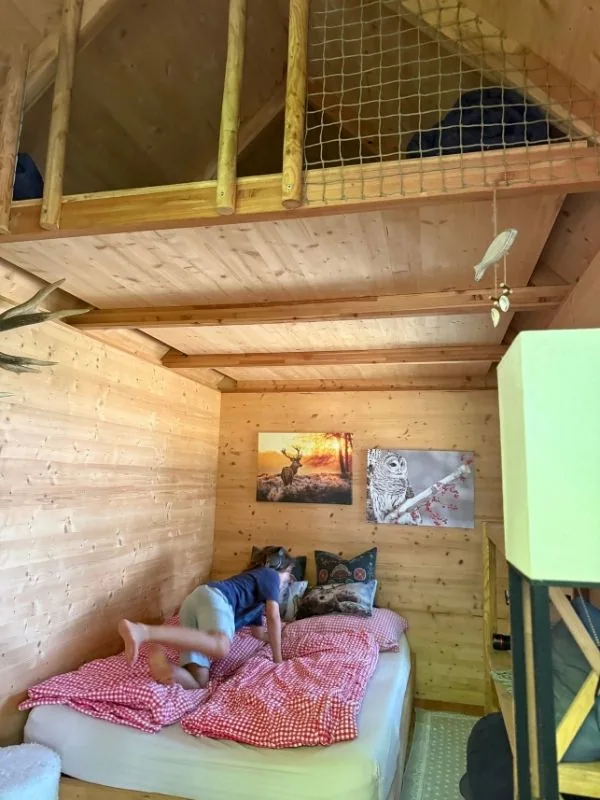 Innenraum des Baumhauses mit Doppelbett und Stauraum im Giebel, erreichbar über eine Leiter