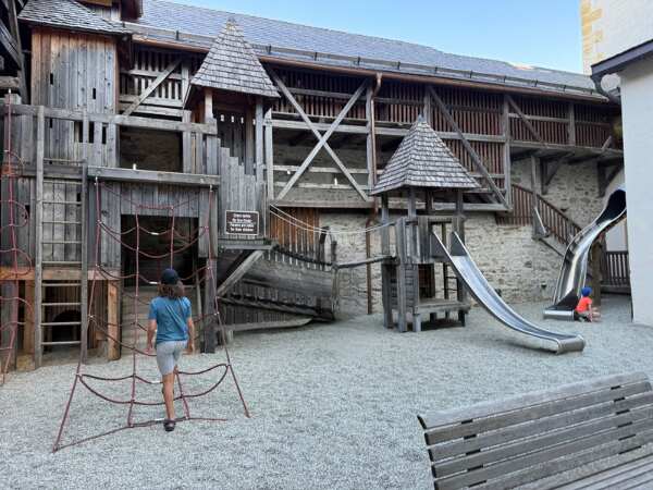 Holzspielplatz mit Kletternetz und Edelstahlrutsche im Innenhof der Burg Mauterndorf