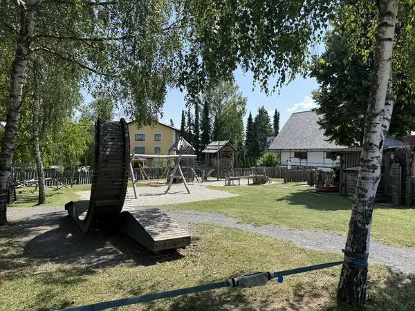 Spielplatz im Park mit Rutsche, Schaukel und Bäumen bei sonnigem Wetter, ideal für Kinder und Familien, in einer ruhigen Wohngegend in Österreich.