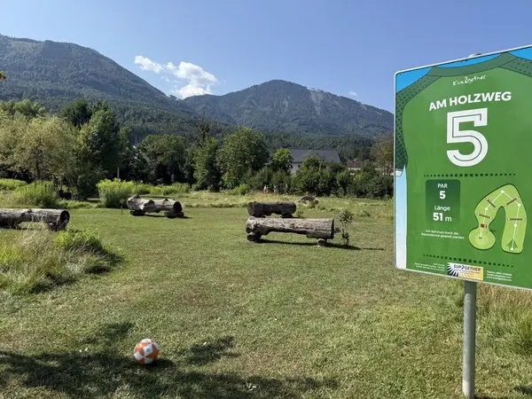 Golfplatz am Holzweg mit Abschlagbereich, Spielbahn und Bergkulisse im Hintergrund, sonniger Tag, Natur und Freizeitgestaltung in der Natur, Österreich.